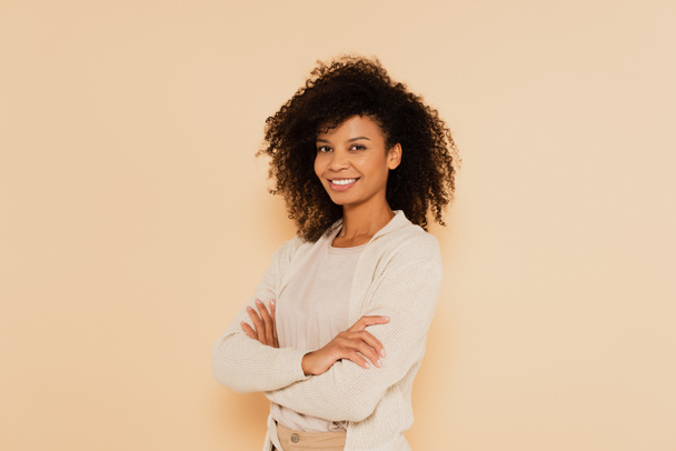 smiling african american woman standing with crossed arms isolated on beige - Photo, Image