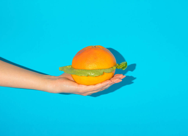 Ženská ruka drží sendvič z grapefruitu a salátu. Abstraktní pojetí nezdravého jídla. Kreativní veganský koncept. - Fotografie, Obrázek