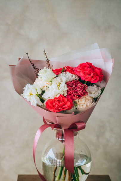 Bright summer bouquet of red roses, burgundy and white carnations, white eustomas in pink packaging. Summer background - Foto, Imagem