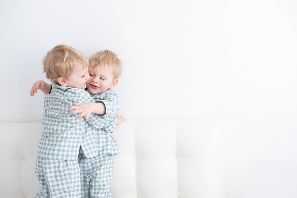 Zwei kleine Zwillingsjungen im Pyjama umarmen sich zu Hause auf weißem Hintergrund. - Foto, Bild