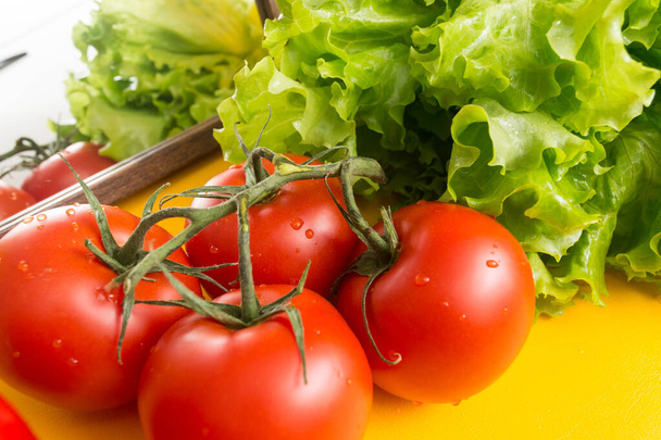 Red tomatoes on a green branch with a large pale. Lettuce leaves in the background. Vegetables for cooking. - Foto, Imagem