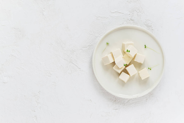Pieces of tofu cheese with micro greens on a light plate. Horizontal orientation, top view, copy space.  - Photo, Image