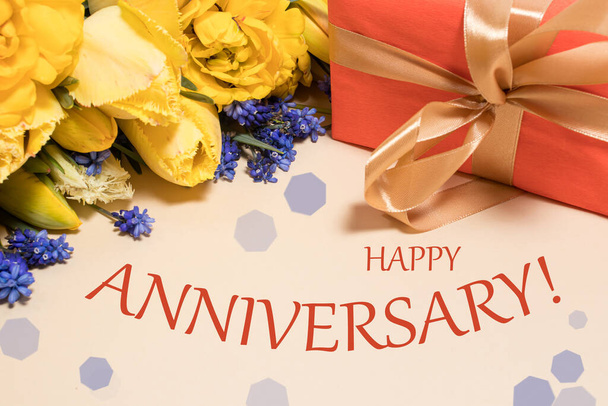 Card with the inscription Happy Anniversary on a background of yellow flowers and red gift. - Photo, Image