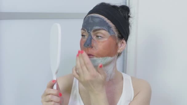 Femme heureuse tenant miroir et examinant masque facial sur son visage - Séquence, vidéo