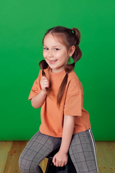 Portrait d'une petite fille souriante avec deux tresses françaises sur fond vert. Le concept d'une enfance heureuse. - Photo, image