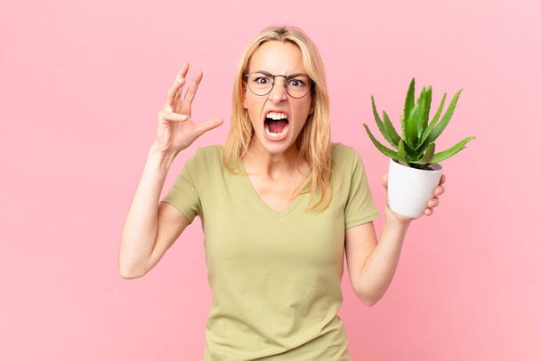 young blonde woman screaming with hands up in the air and holding a cactus - Fotó, kép