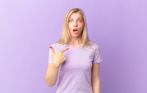 young blonde woman looking shocked and surprised with mouth wide open, pointing to self - Foto, immagini