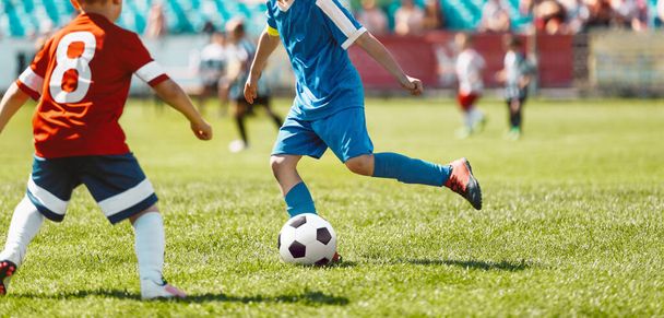 Kinderen spelen de wedstrijd op voetbalstadion veld. Jongens doen mee aan een voetbaltoernooi. Kinderen in rode en blauwe voetbalshirts - Foto, afbeelding