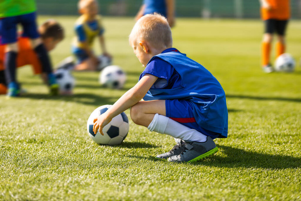 Boldog gyermek sportuniformisban, labdával a füvön. Gyerekek foci órán a futball nyári táborban - Fotó, kép