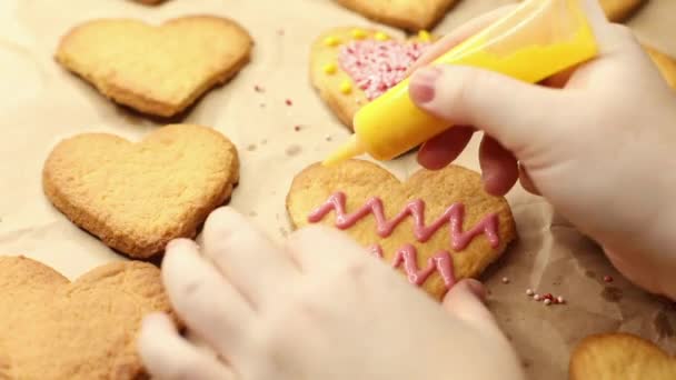 donna decora biscotti a forma di cuore con glassa gialla, primo piano, processo di cottura, concetto romantico - Filmati, video