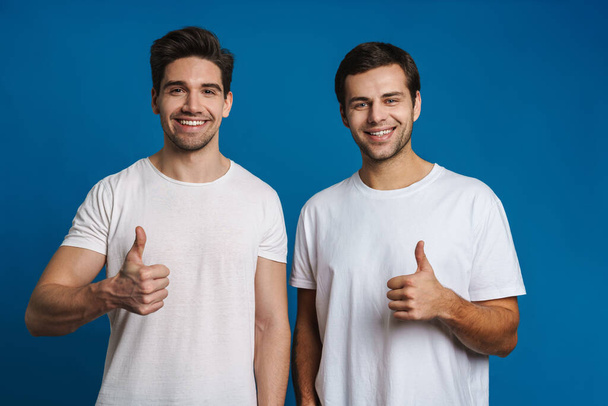 Joyful handsome guys smiling and showing thumbs up isolated over blue background - Foto, imagen