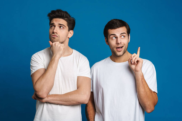 Caucasian two guys looking and pointing finger upward isolated over blue background - Foto, Bild