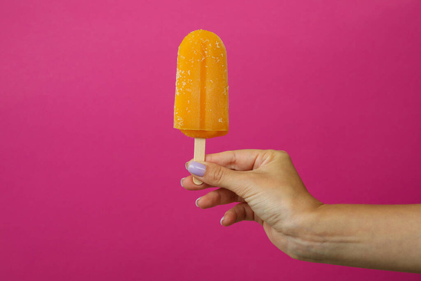 Female hand hold ice cream stick on pink background - Foto, Imagen