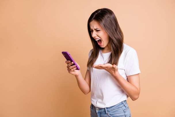 Photo portrait of mad furious girl shouting keeping cellphone angry crazy isolated pastel beige color background - Zdjęcie, obraz