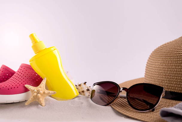 Sunscreen spray bottle and summer straw hat beach shoes and sunglasses against cloudy sky. Summer vacation concept. - Photo, Image