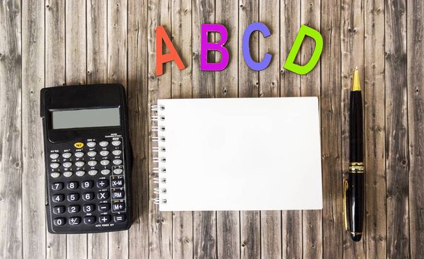 lettres alphabétiques de couleur bois reposent sur une table brune, à côté d'un carnet pour l'écriture, une calculatrice et un stylo - Photo, image