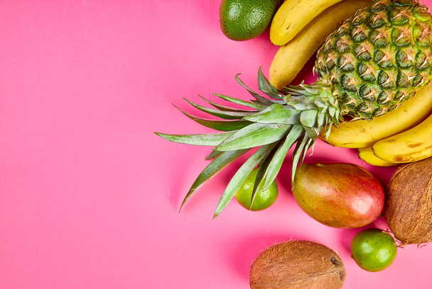 Flat lay of exotic fruits on pink background - mango, pineapple, banana, avocado, coconut, lime. Top view. Creative layout made of tropical fruits, copy space, summer concept. - Photo, image