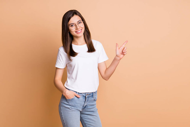 Foto portret van vrouwelijke student in brillen wijzende vinger blanco ruimte aanbevelen geïsoleerde pastel beige kleur achtergrond - Foto, afbeelding