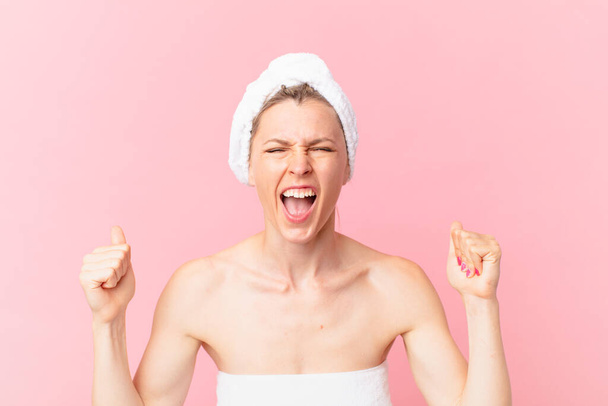 young blonde woman shouting aggressively with an angry expression and after shower - Foto, imagen