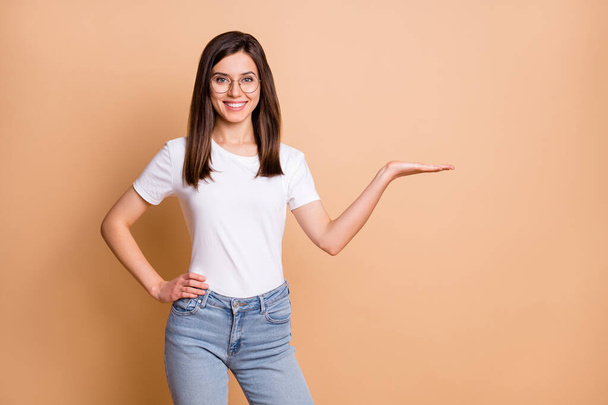 Photo portrait of female student wearing glasses holding empty space on hand smiling casual clothes isolated pastel beige color background - Φωτογραφία, εικόνα