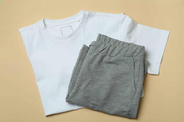 T-shirt και φόρμες σε μπεζ φόντο, top view - Φωτογραφία, εικόνα