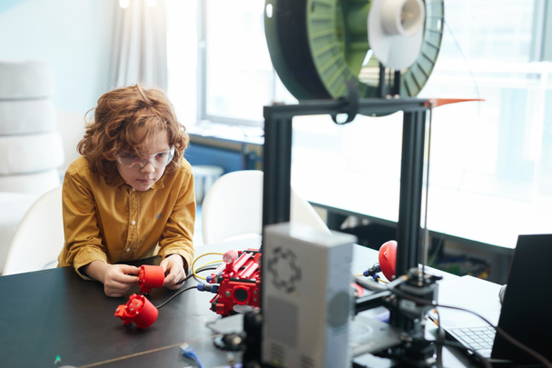 Portrait of cute curly haired boy building robot boat during engineering class at modern school, copy space - Foto, Imagem