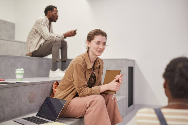 Ritratto laterale di giovane studentessa che chiacchiera con gli amici mentre si rilassa nella moderna sala della scuola, copia lo spazio - Foto, immagini