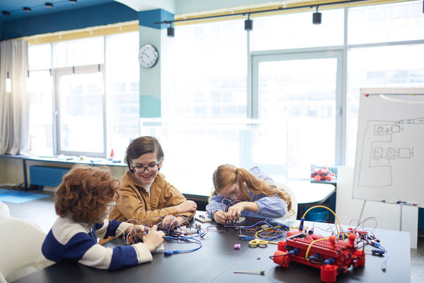 Ritratto grandangolare di tre bambini che costruiscono robot durante la lezione di ingegneria nella scuola di sviluppo, copia lo spazio - Foto, immagini