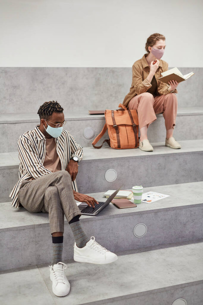 Vertical full length portrait of two young students working and relaxing while sitting in graphic college lounge - Fotó, kép