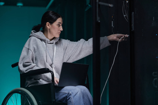 Visão lateral retrato de mulher com deficiência em cadeira de rodas trabalhando com rede de supercomputadores na sala de servidores, conceito de trabalho acessível, espaço de cópia - Foto, Imagem