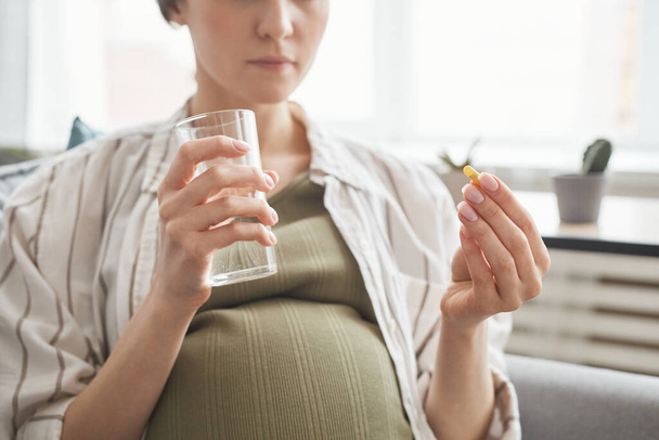 Nahaufnahme einer schwangeren Frau, die morgens ein Glas mit Wasser hält und Vitamine trinkt - Foto, Bild