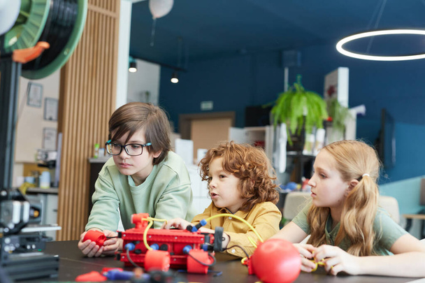 Portrait de trois enfants opérant des robots pendant les cours d'ingénierie à l'école moderne, espace de copie - Photo, image