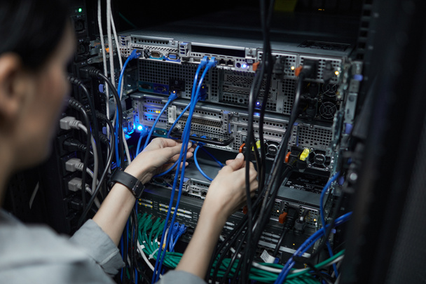 Close up of female network technician connecting cables in server cabinet while setting up supercomputer at data center, copy space - Foto, Imagen