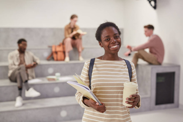 Waist up portrait of female African-American student smiling at camera while posing in modern school lounge, copy space - Photo, image