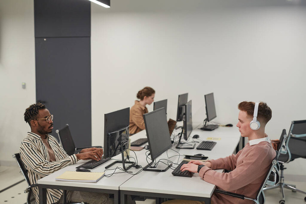 Широкий кут зору на групу молодих людей, які використовують комп'ютери під час роботи в офісній або шкільній ІТ-лабораторії, простір для копіювання
 - Фото, зображення