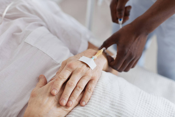 Close-up van Afro-Amerikaanse mannelijke verpleegkundige opzetten IV druppelen tijdens het verzorgen van senior man in het ziekenhuis, kopiëren ruimte - Foto, afbeelding