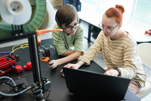 Visão de alto ângulo em jovem professora ajudando menino usando impressora 3D durante a aula de robótica e engenharia na escola - Foto, Imagem