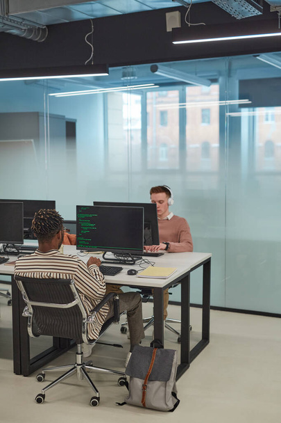 Κατακόρυφο πλήρες μήκος προγραμματιστών πληροφορικής ή φοιτητών που χρησιμοποιούν υπολογιστές στο εσωτερικό του γραφείου με γυάλινο τοίχο, αντιγραφή χώρου - Φωτογραφία, εικόνα
