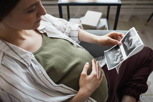 妊娠中の女性はソファに座って休んでいます彼女はX線画像を見て、彼女の赤ちゃんの誕生を待っています - 写真・画像