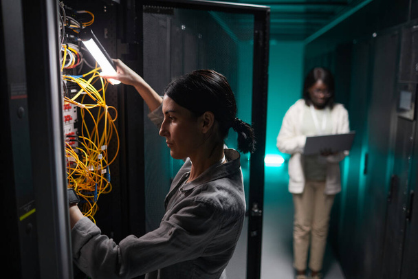 Ritratto laterale di ingegnere di rete femmina che collega i cavi nell'armadio del server mentre lavora con il supercomputer nel data center, copia lo spazio - Foto, immagini
