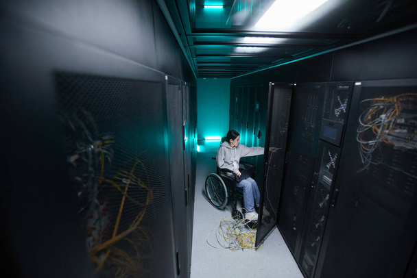 Ευρεία γωνία πορτρέτο της γυναίκας με ειδικές ανάγκες σε αναπηρική καρέκλα που εργάζονται με το δίκτυο υπερυπολογιστών στο δωμάτιο διακομιστή, προσβάσιμη έννοια της εργασίας, αντίγραφο χώρου - Φωτογραφία, εικόνα