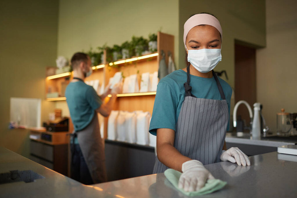 Retrato de jovem afro-americana barra de limpeza contador com desinfetante enquanto trabalhava em café ou café, medidas de segurança vívidas, espaço de cópia - Foto, Imagem