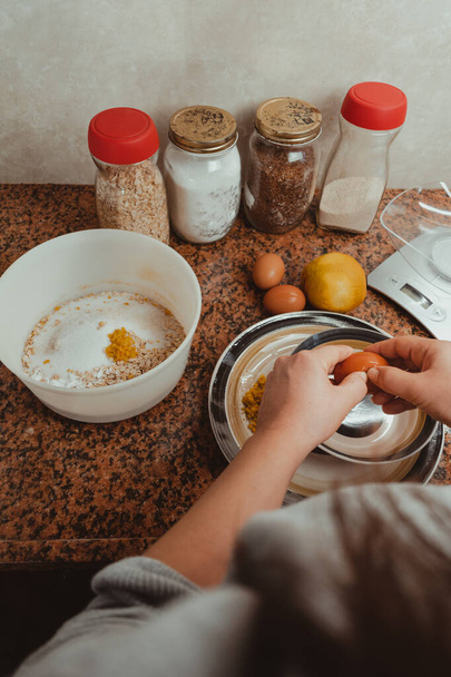 Крупный план женской руки, разбивающей яйцо, которое она добавит в смесь печенья. Концепция здорового образа жизни и домашней пищи. - Фото, изображение