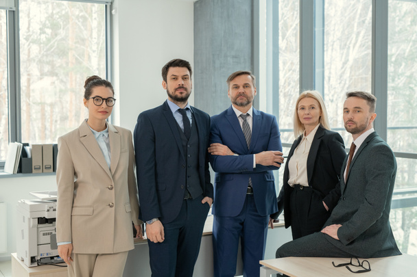 Team of confident lawyers in suits standing together in office and looking at camera - Valokuva, kuva