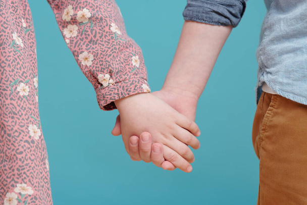 Detailní záběr malého chlapce a holčičky držící se za ruce na modrém pozadí - Fotografie, Obrázek