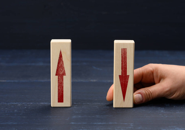 female hand holds a wooden block with an upward arrow and down arrow. Concept of increasing profit growth, increasing bank interest on deposits, blue background - Photo, Image