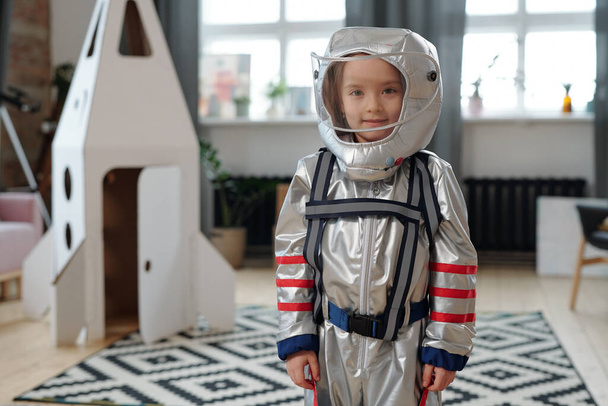 Porträt eines kleinen Mädchens im Astronautenkostüm, das beim Spielen im Zimmer in die Kamera lächelt - Foto, Bild