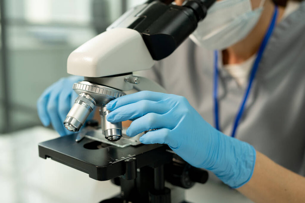 Close-up of unrecognizable lab employee in blue gloves adjusting microscope slide in laboratory while doing research - Foto, imagen