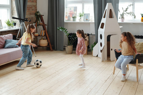 Grupa małych dziewczynek grających razem w piłkę nożną w pokoju w domu - Zdjęcie, obraz