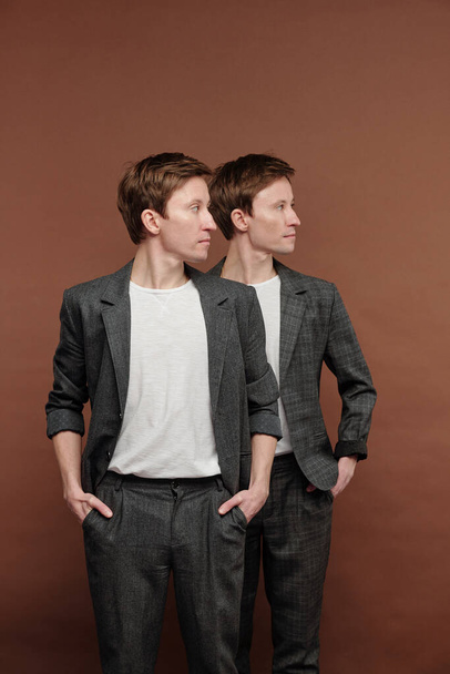Selbstbewusste junge Zwillingsbrüder in grauen Anzügen stehen sich gegenüber und blicken in die Ferne - Foto, Bild